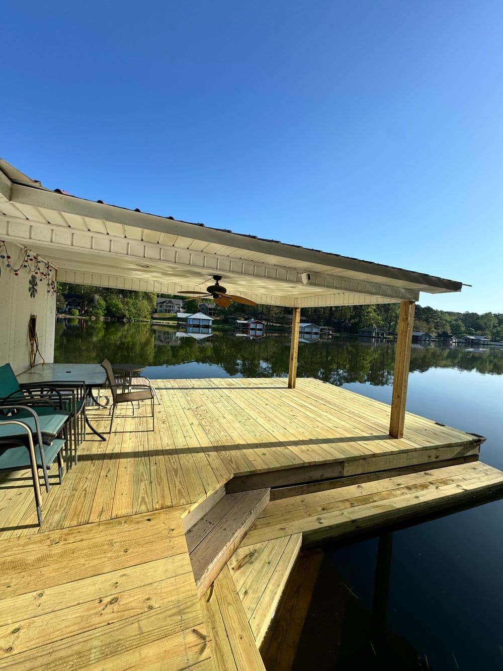Lakeside deck with seating, sunny sky, and reflections on calm water. Perfect for relaxation.