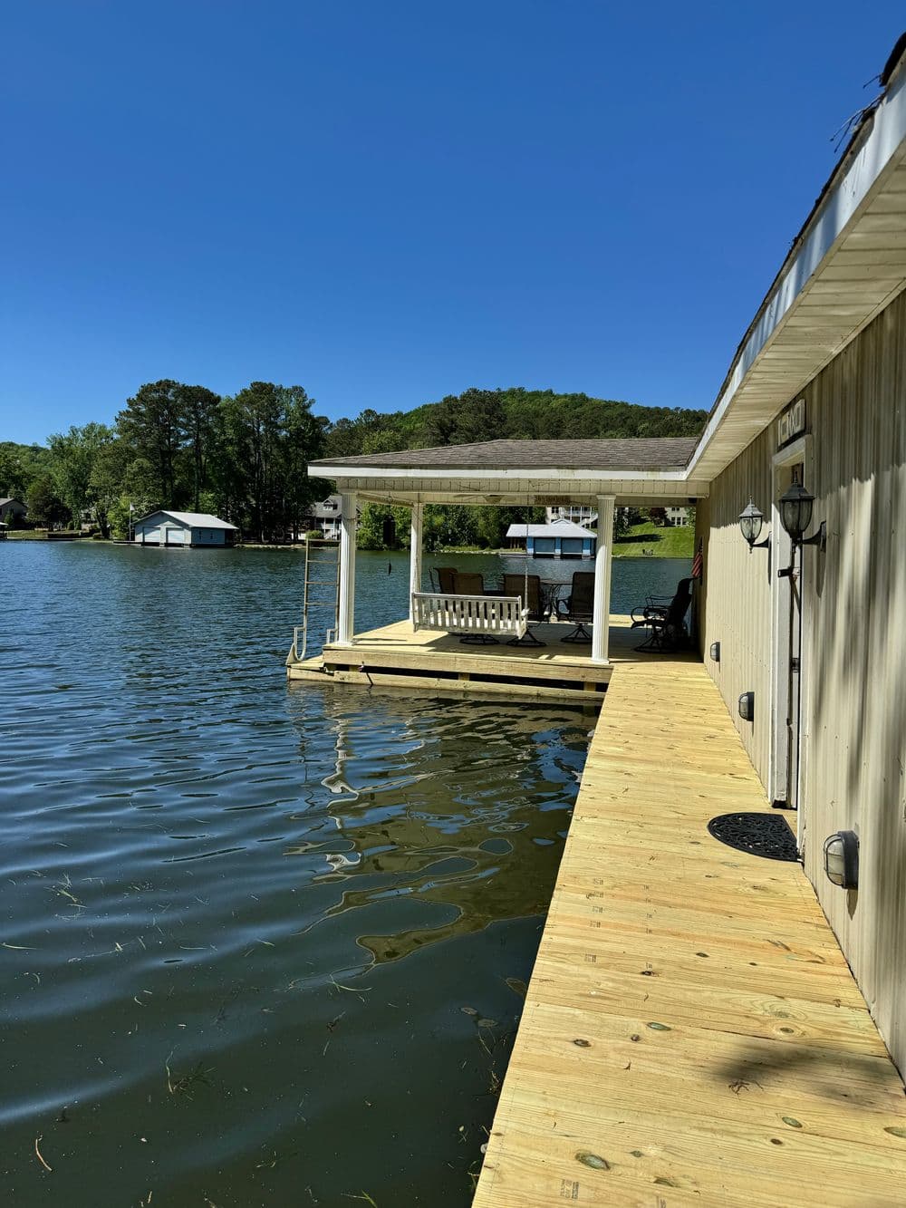 Scenic lakeside view with a dock and home under blue sky and lush greenery.