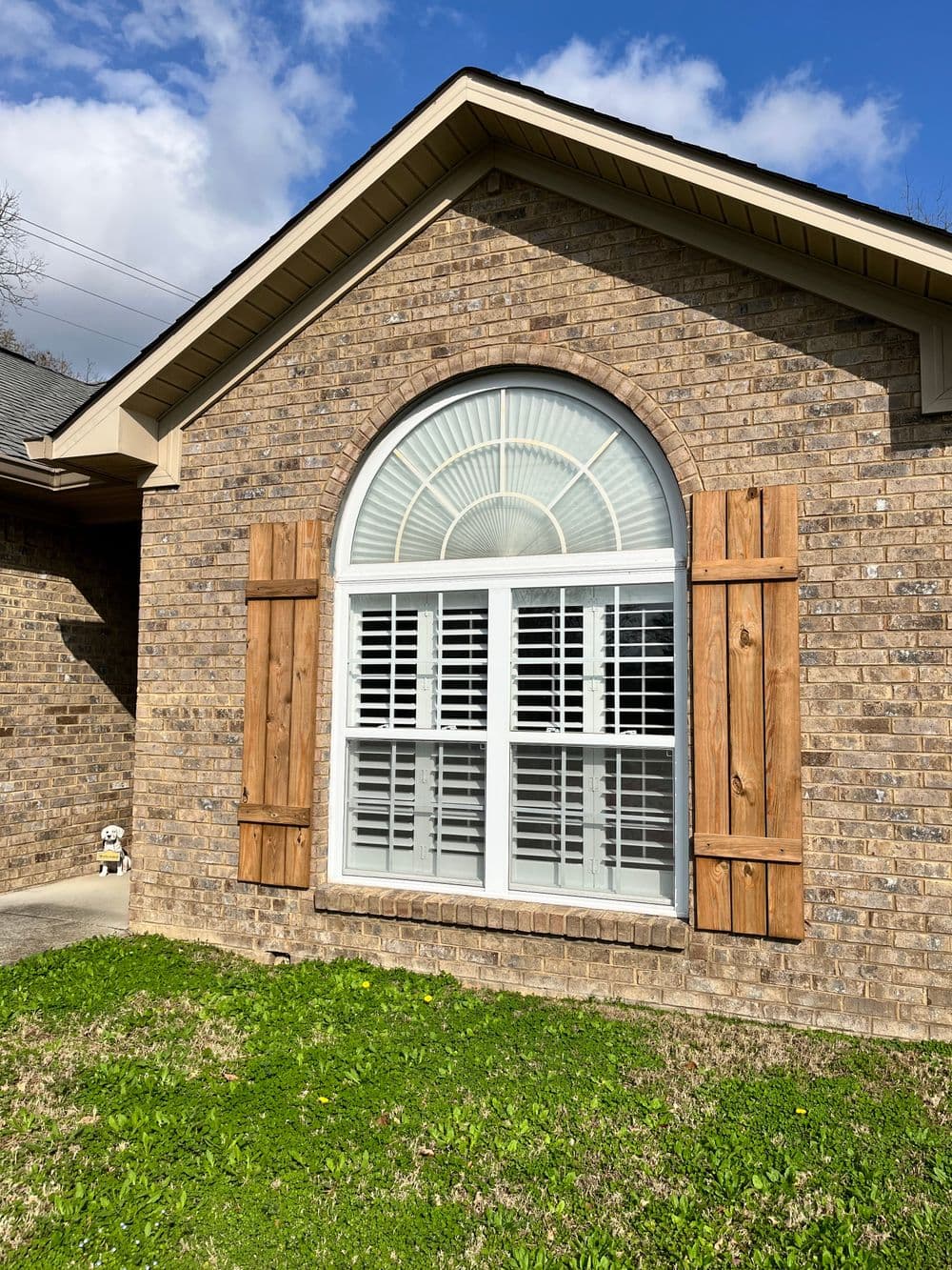Brick home with arched window, wooden shutters, and green grass under a blue sky.