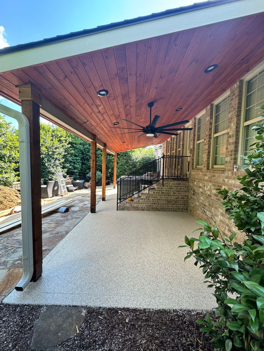 Covered outdoor patio with wooden ceiling, ceiling fan, and stone stairway.