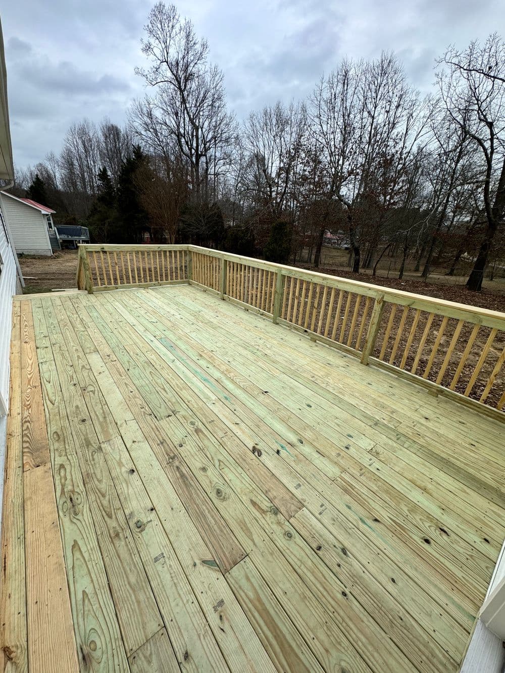 Newly constructed wooden deck with railings surrounded by trees under a cloudy sky.