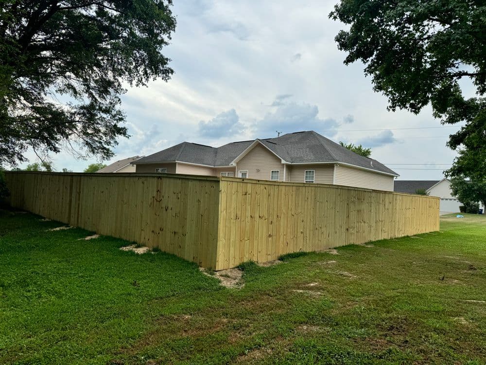 Wooden fence surrounding a landscaped yard with houses in the background under a cloudy sky.