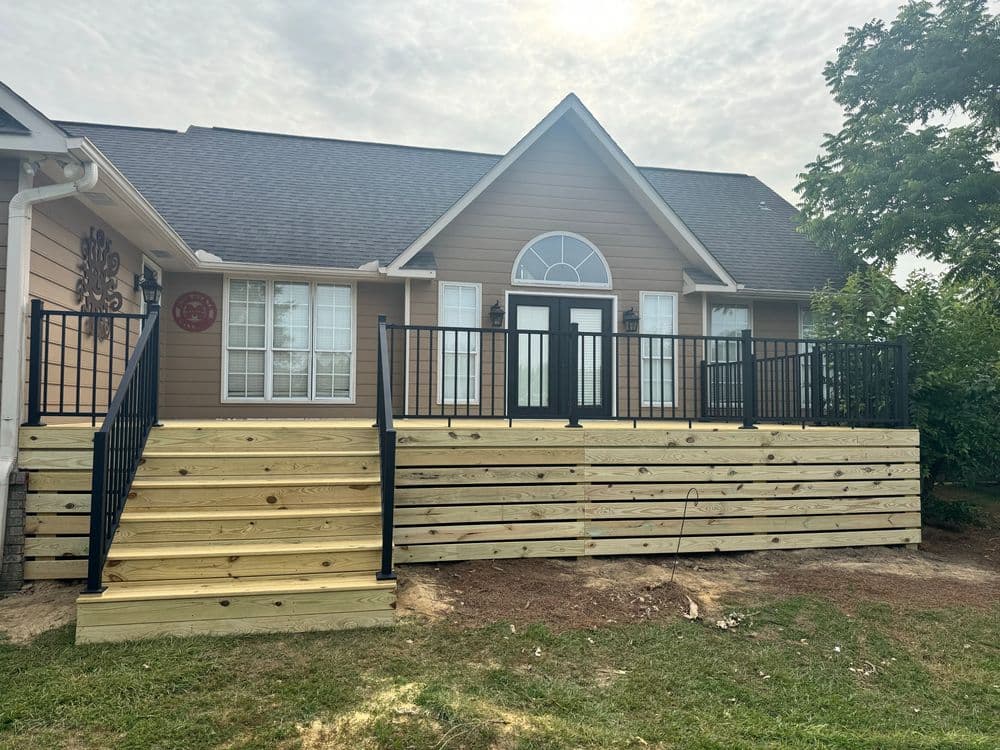 New wooden deck with black railing in front of a beige house with large windows.