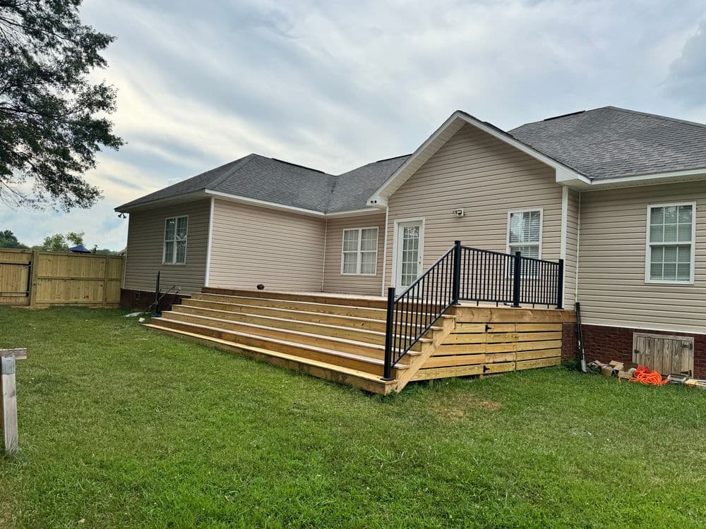 Single-story home with a wooden deck and fenced yard under a cloudy sky.