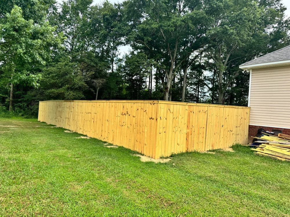 Wooden privacy fence in a grassy yard surrounded by trees and a house.