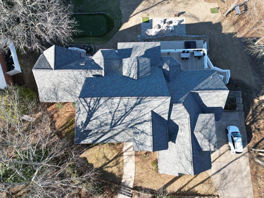 Aerial view of a modern home with multiple sloped roofs, surrounded by trees and outdoor space.