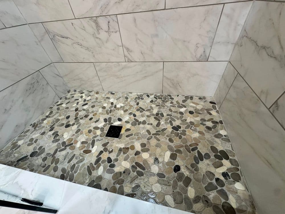 Luxury shower with marble walls and pebble stone floor in modern bathroom design.