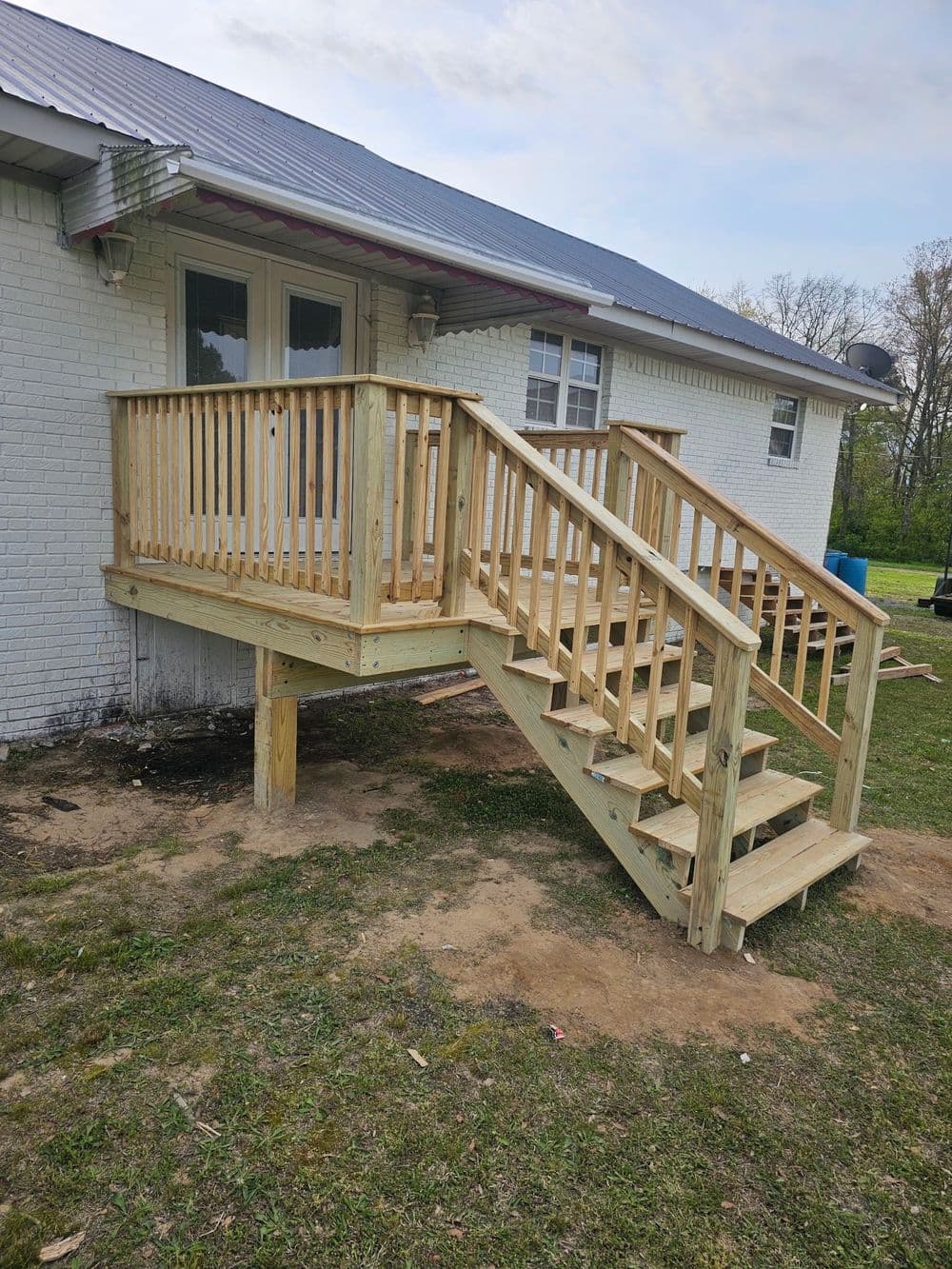 Exterior wooden deck with stairs and railing, attached to a white brick house.