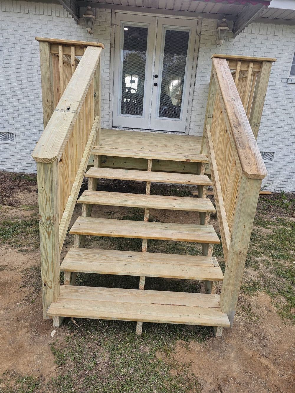 Newly built wooden stairs leading to a white house with double doors.